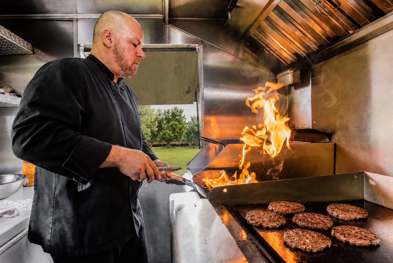 Chef Alex searing burger patties over the flames on the Latin Fixin's food truck grill